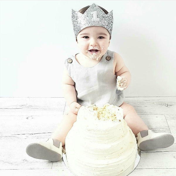 cake smash crown in silver glitter and pale grey shown on a 1 year old boy eating cake for a cake smash photoshoot